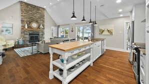 Une cuisine spacieuse dotée d’un îlot central, d’une cheminée en pierre et de luminaires suspendus.