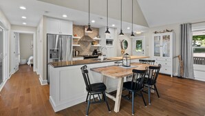 Une cuisine moderne avec des meubles blancs, un îlot central en bois et des luminaires suspendus.
