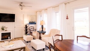 Un salon avec une cheminée, un téléviseur et un coin repas comprenant une table et des chaises.