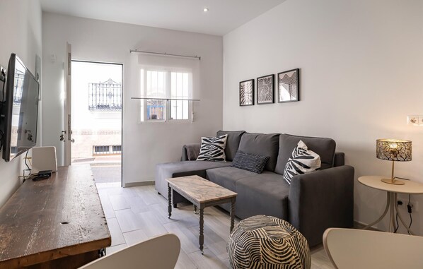 A modern living room with a grey sofa, a wooden coffee table, and a round side table with a lamp. There are three framed artworks on the wall and a television mounted on the wall.