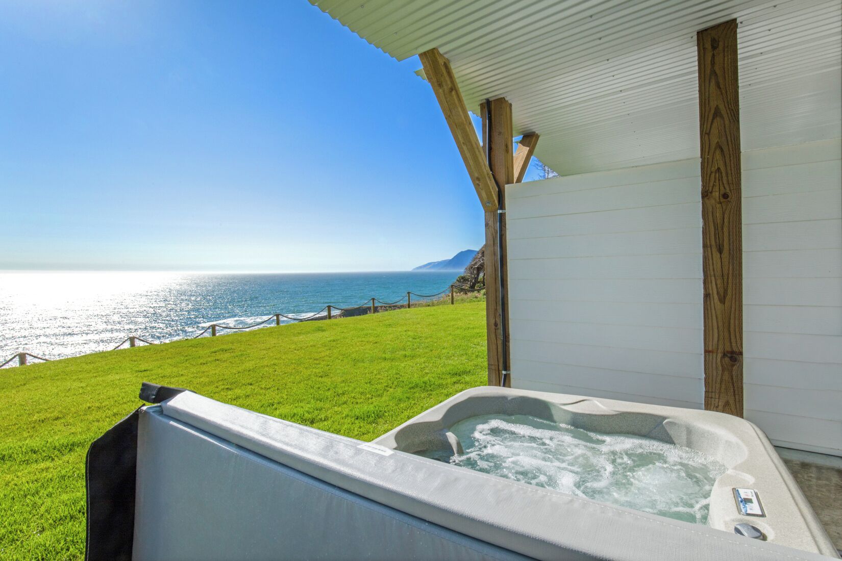 A hot tub with a view of the ocean and a grassy area.