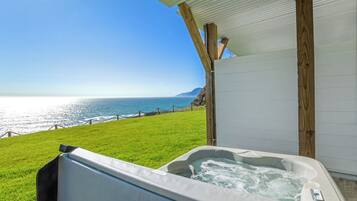 A hot tub with a view of the ocean and a grassy area.