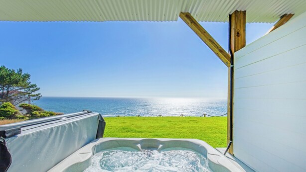 A hot tub with a view of the ocean and a grassy area. - Seagull by OceanviewHotTubs Oceanfront Tesla charging Oceanfront Shelter Cove (Whitethorn)