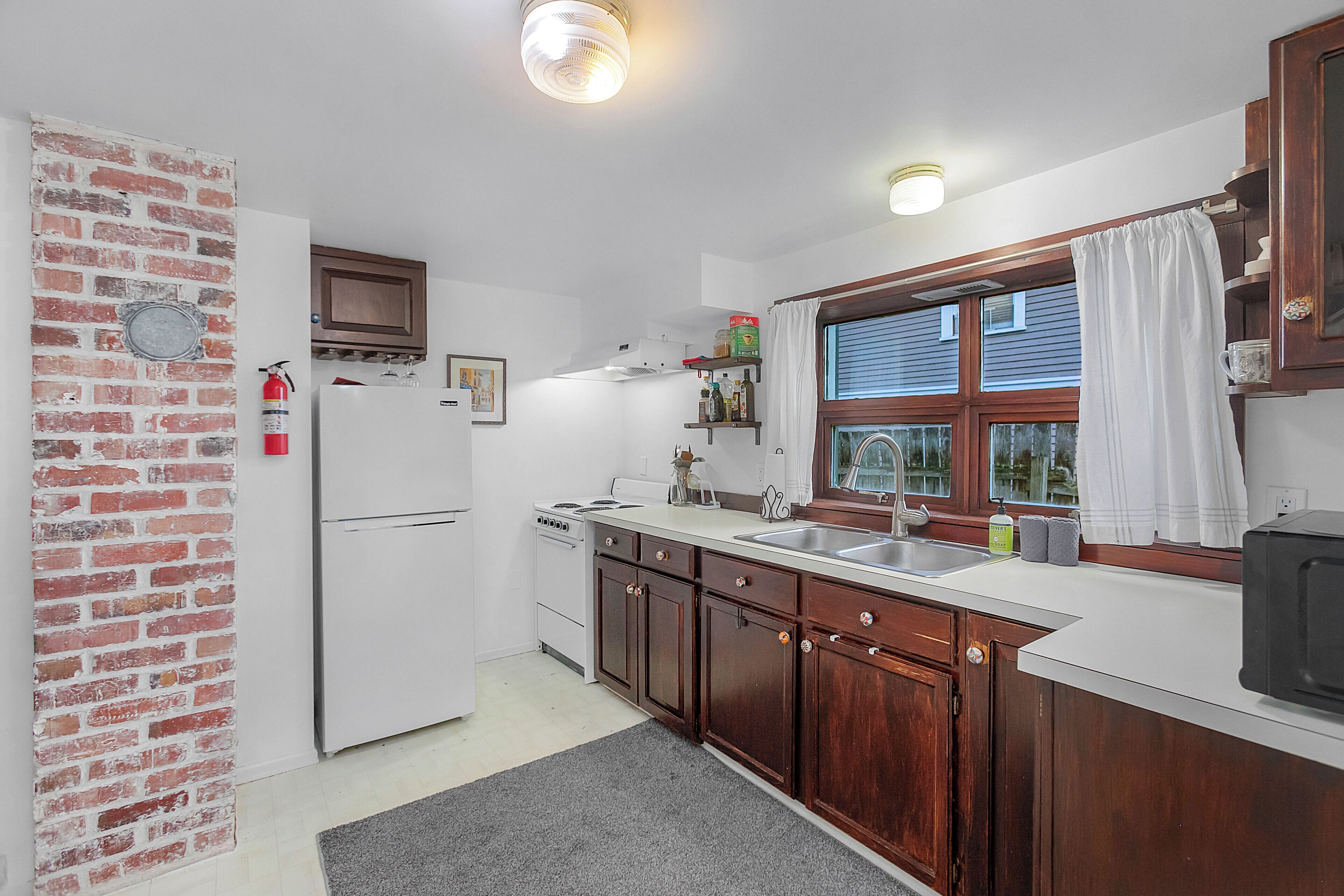 A kitchen with wooden cabinets, a white refrigerator, a stove, and a window with curtains.