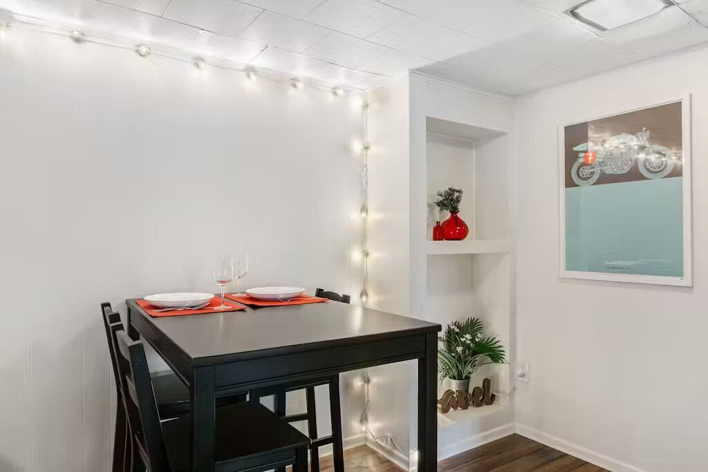 Un comedor con una mesa de madera oscura, paredes blancas y luces colgantes.