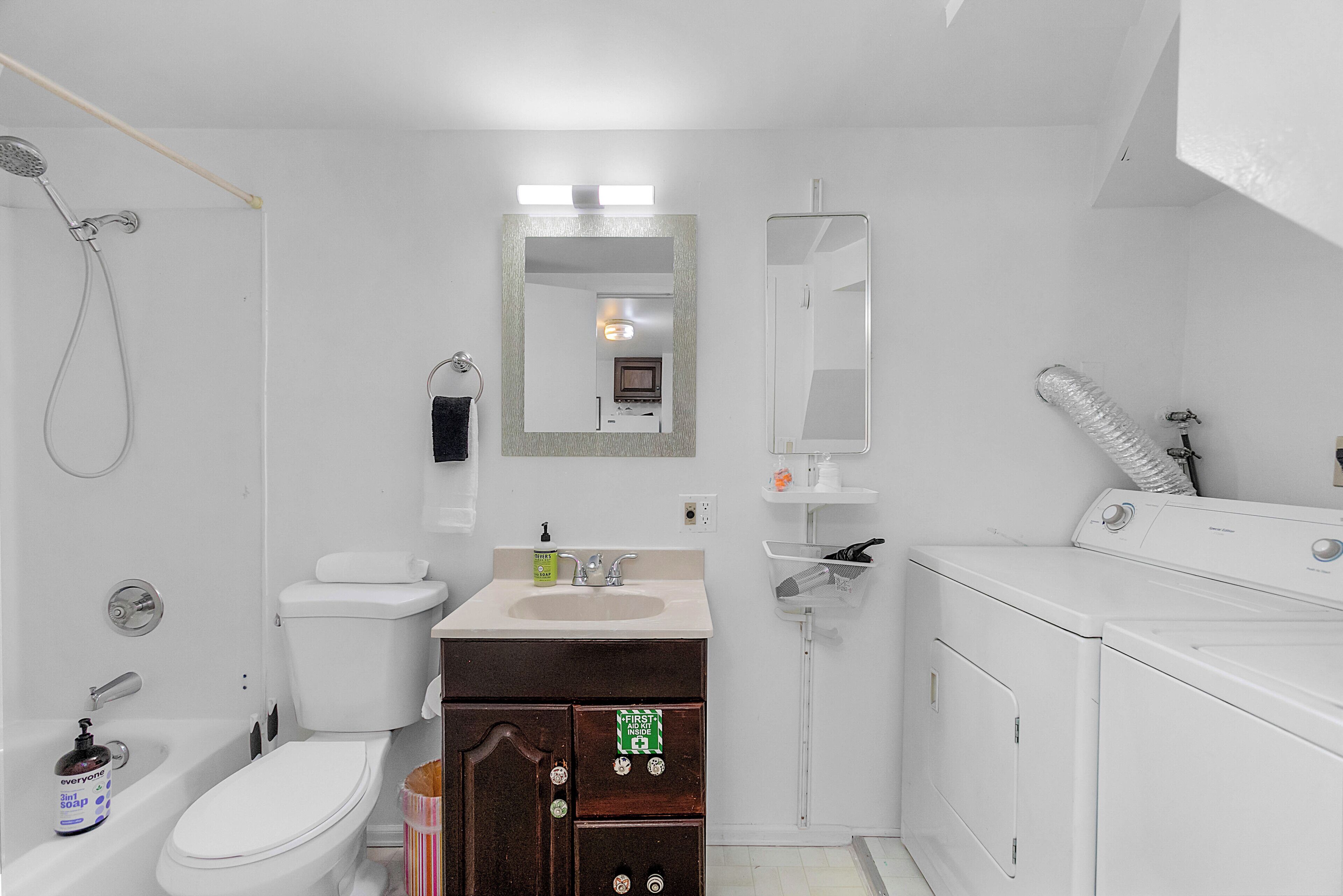 Un baño con inodoro, lavamanos, espejo, ducha y lavadora.