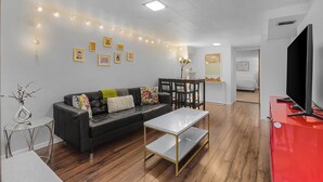 A modern living room with a black leather sofa, a white coffee table, and a red entertainment unit. - Green Lake Zen Low Level Garden Suite (Seattle)