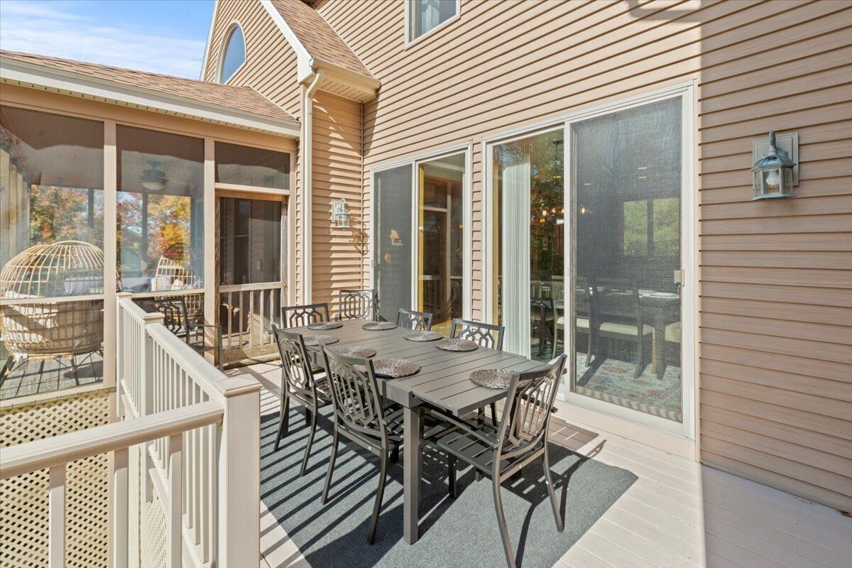 A patio with a dining table and chairs, large windows, and a wooden deck.
