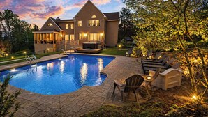 A swimming pool with a deck, surrounded by outdoor furniture and a large house.