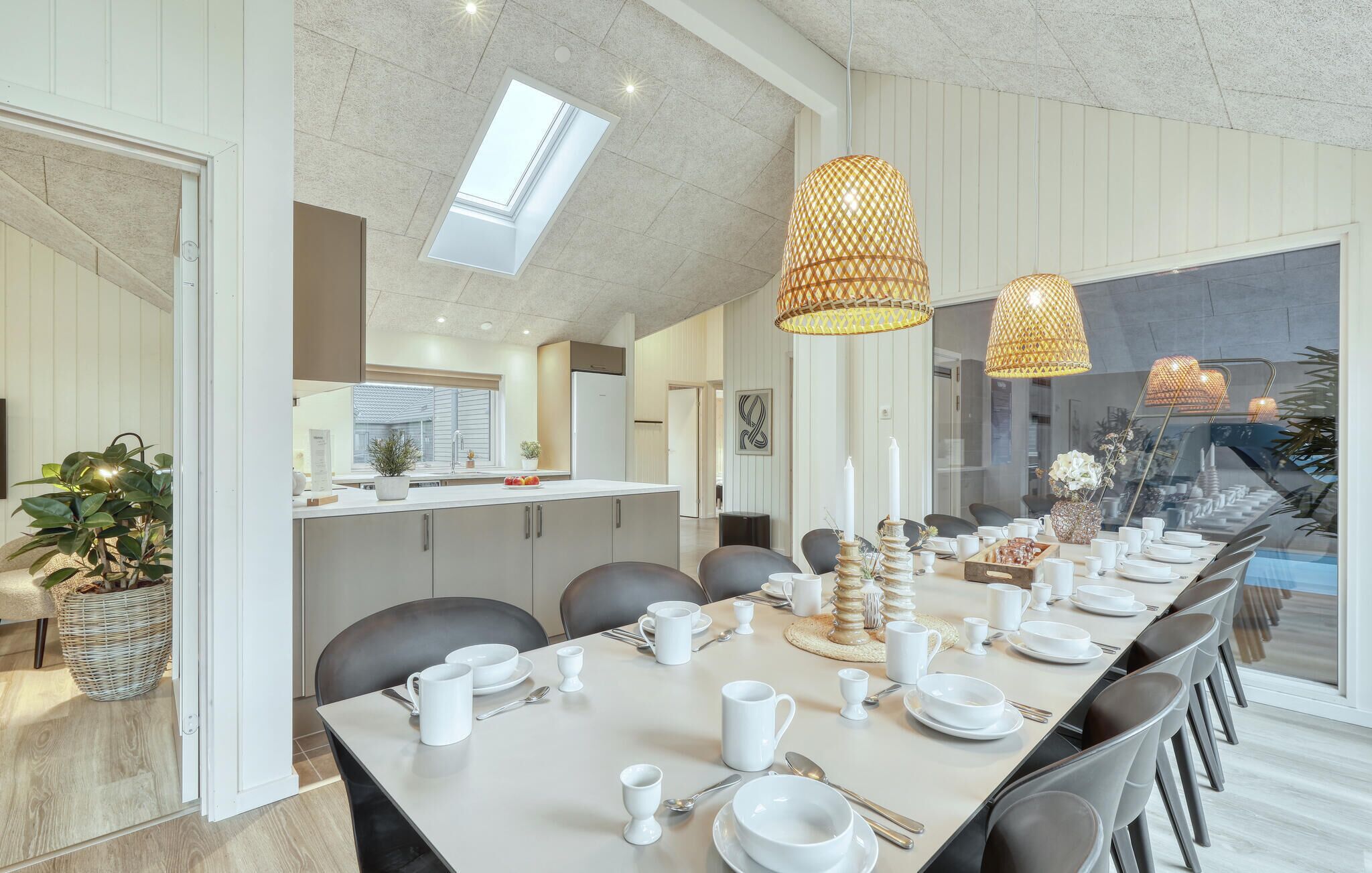 A modern dining area with a long table set for a meal, featuring a variety of white dishes and cups.