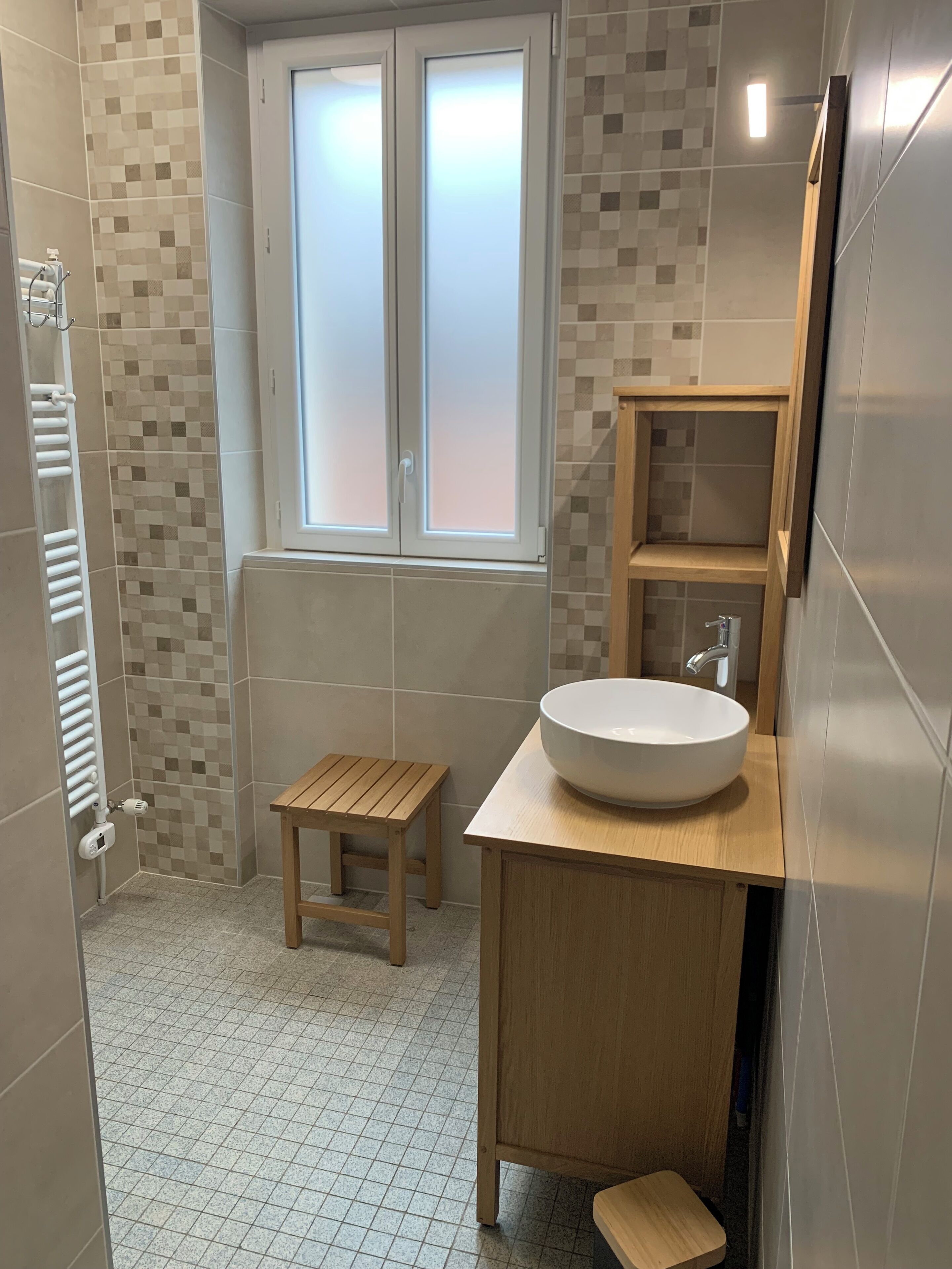 Ein modernes Badezimmer mit großem Fenster, einem Holzhocker, einem weißen Waschbecken und einem Handtuchhalter.