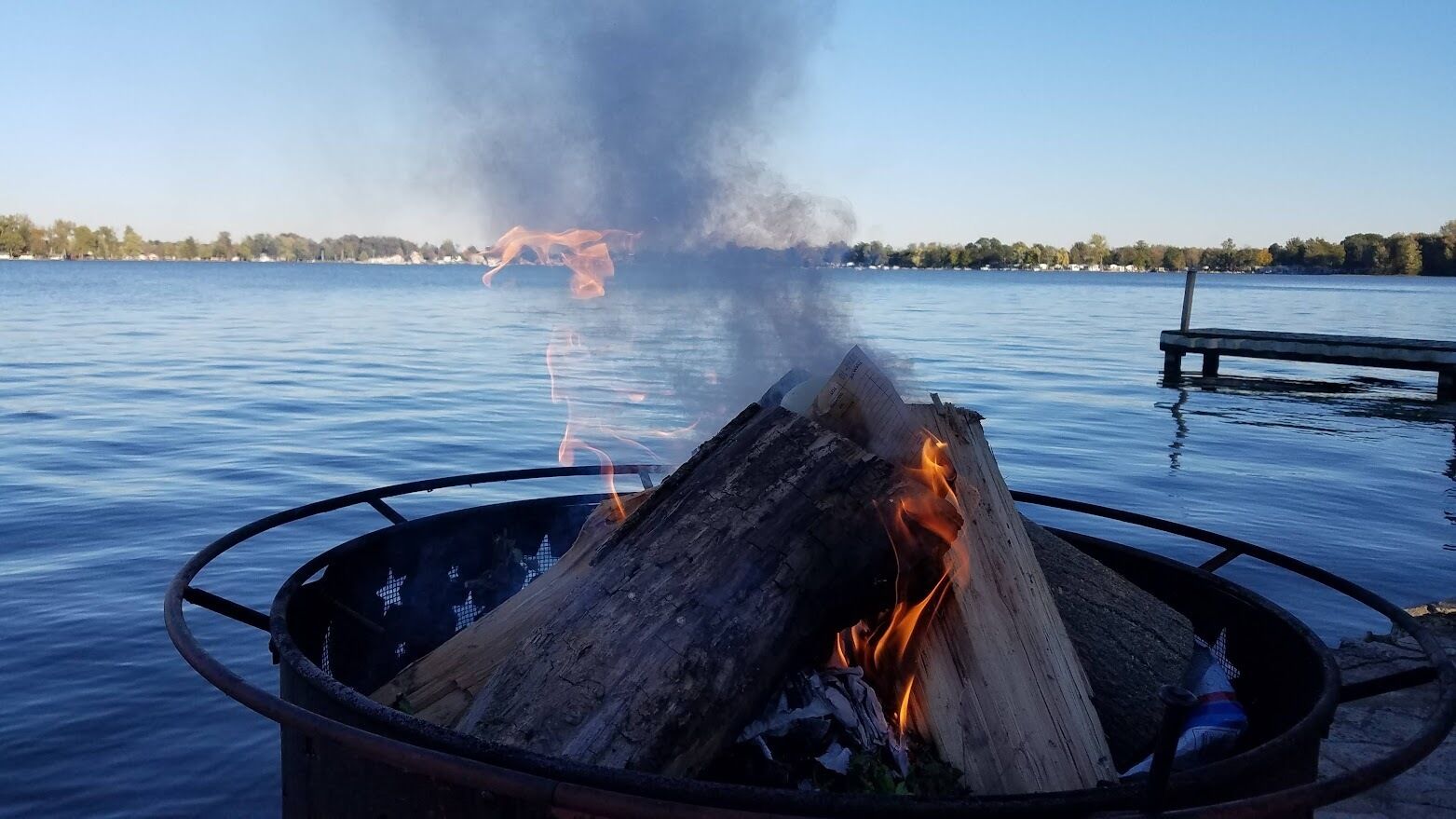 Ein Lagerfeuer in einem Metall-Feuerkorb am Seeufer.