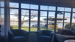 A room with large windows offering a view of a lake and buildings. There are two armchairs and a sofa.