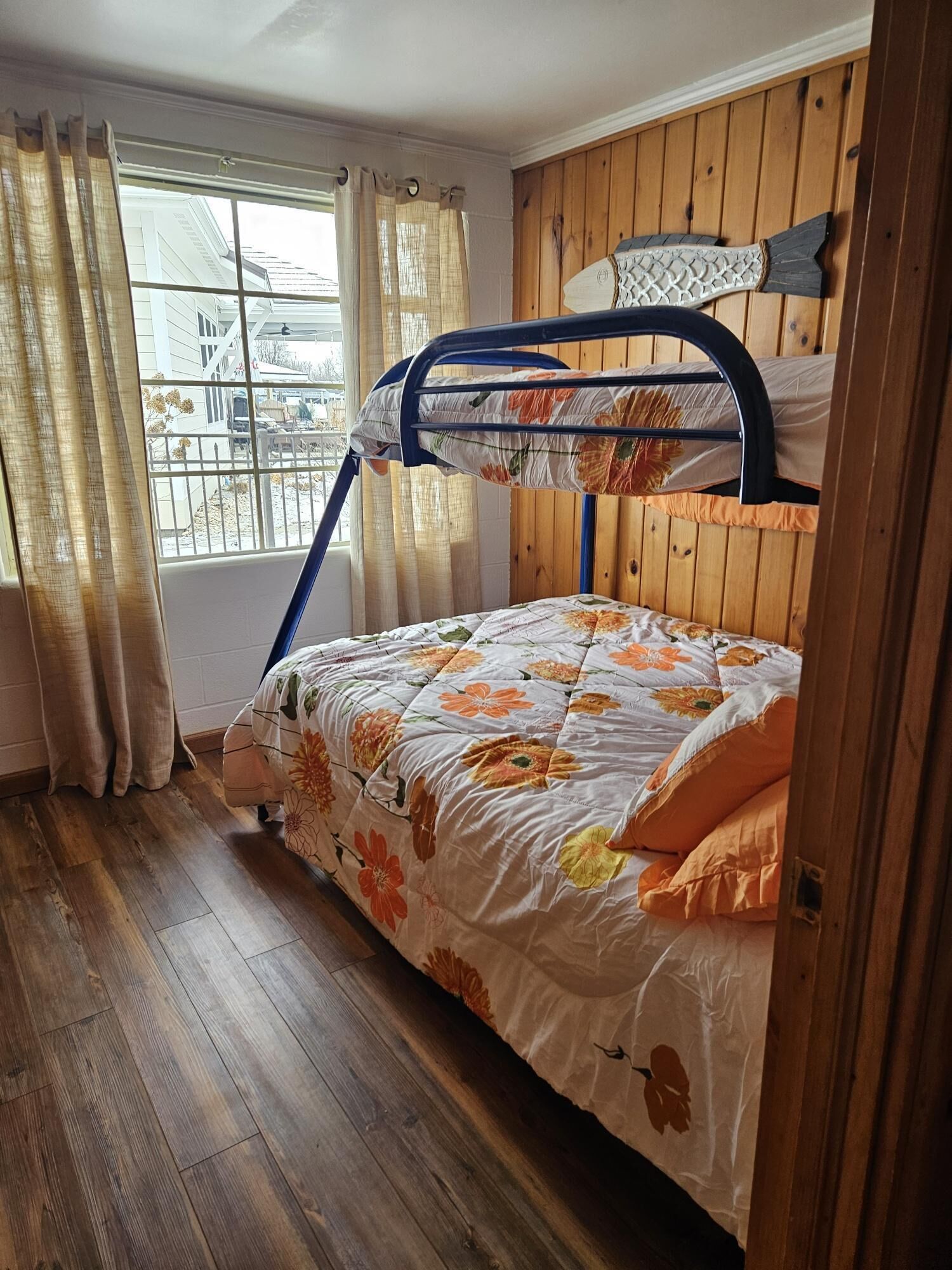 A bunk bed with floral bedding, wooden walls, and a window with curtains.