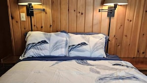 A bed with a floral bedspread, two wall-mounted lamps, and wooden paneling on the wall.