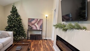 A living room with a Christmas tree, a fireplace, a flat-screen TV, and a painting on the wall. - Beach house - 2 min from Conimicut Beach (Warwick)