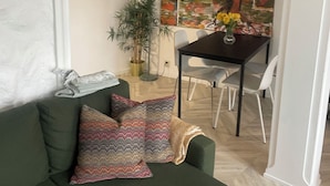 A living room with a green sofa, patterned cushions, a small table with a vase of yellow flowers, and a large abstract painting on the wall. - City View Bergen. City and sea views from your private terrace. Very central.  (Vestland)