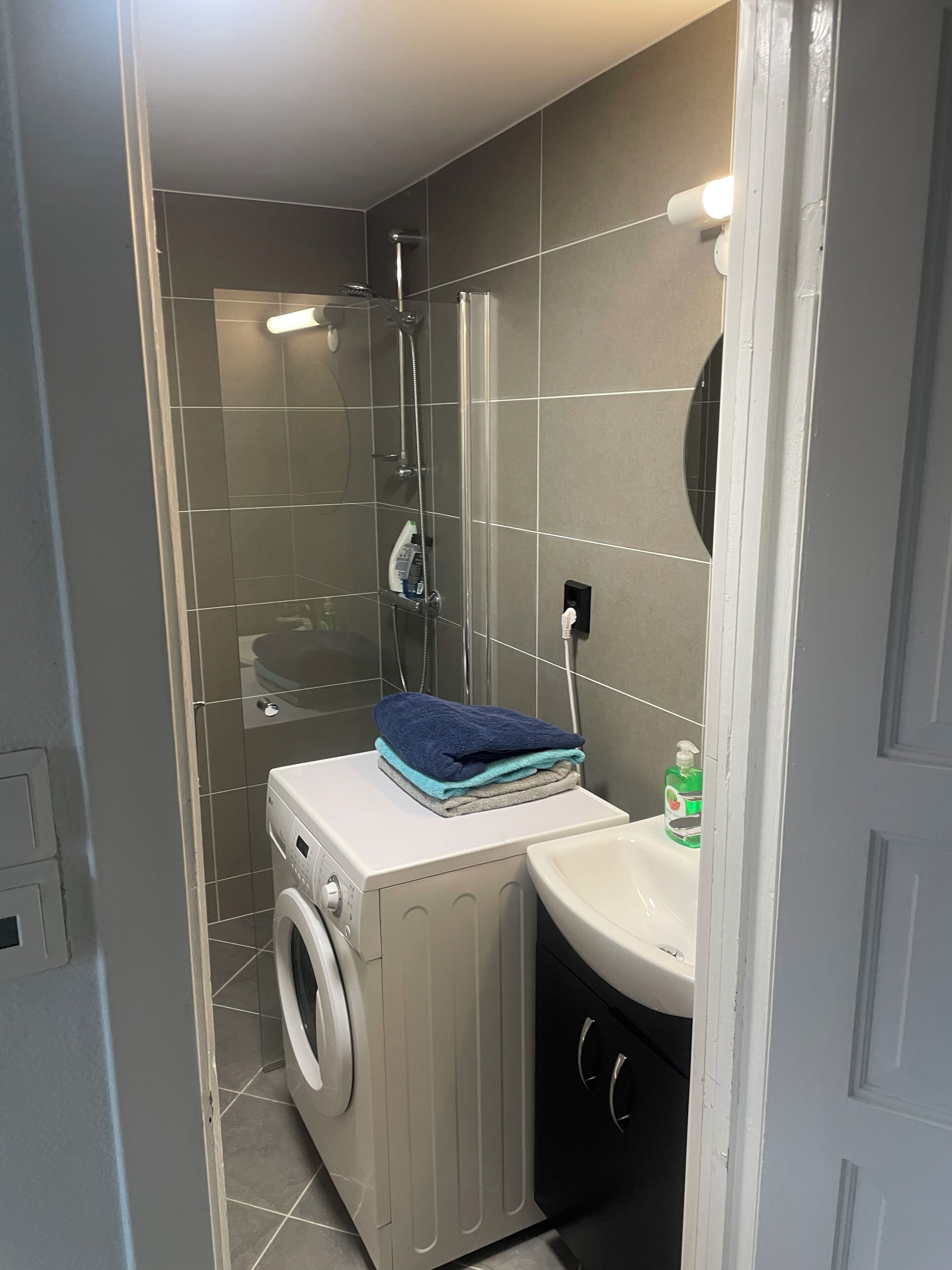 Une petite salle de bain équipée d’un lave-linge, d’un lavabo et d’un espace douche.