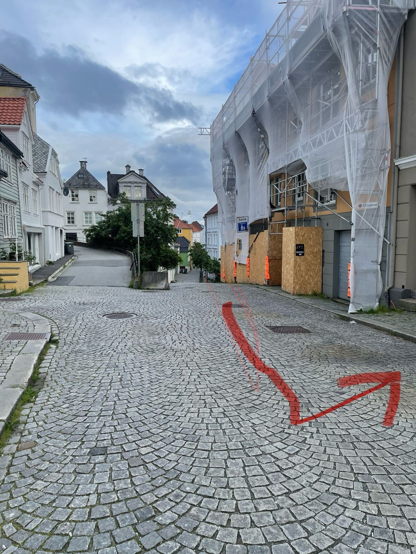 En kullerstensgata med byggnader på båda sidor, varav några är under renovering och har ställningar runt sig.