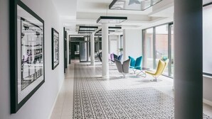 Un interior moderno con piso estampado, paredes blancas y un largo pasillo con cuadros enmarcados.