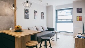 Un espacio habitable moderno con una mesa de comedor de madera, un sofá gris y una pequeña mesa redonda. Hay cuadros enmarcados en la pared y un gran ventanal que proporciona luz natural.