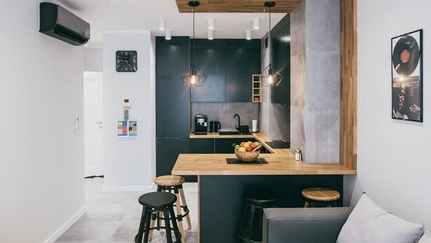 Una cocina moderna con isla de madera, armarios negros e iluminación colgante.