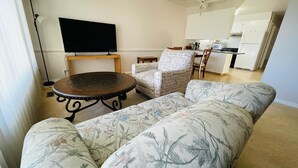 Een woonkamer met een bank, een ronde salontafel, een televisie en een keuken op de achtergrond.