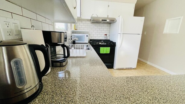 Een keuken met waterkoker, koffiezetapparaat, magnetron, fornuis en koelkast.