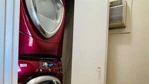 Een wasserette met een rode voorlader wasmachine en droger, een witte deur en een luchtventiel aan de muur.