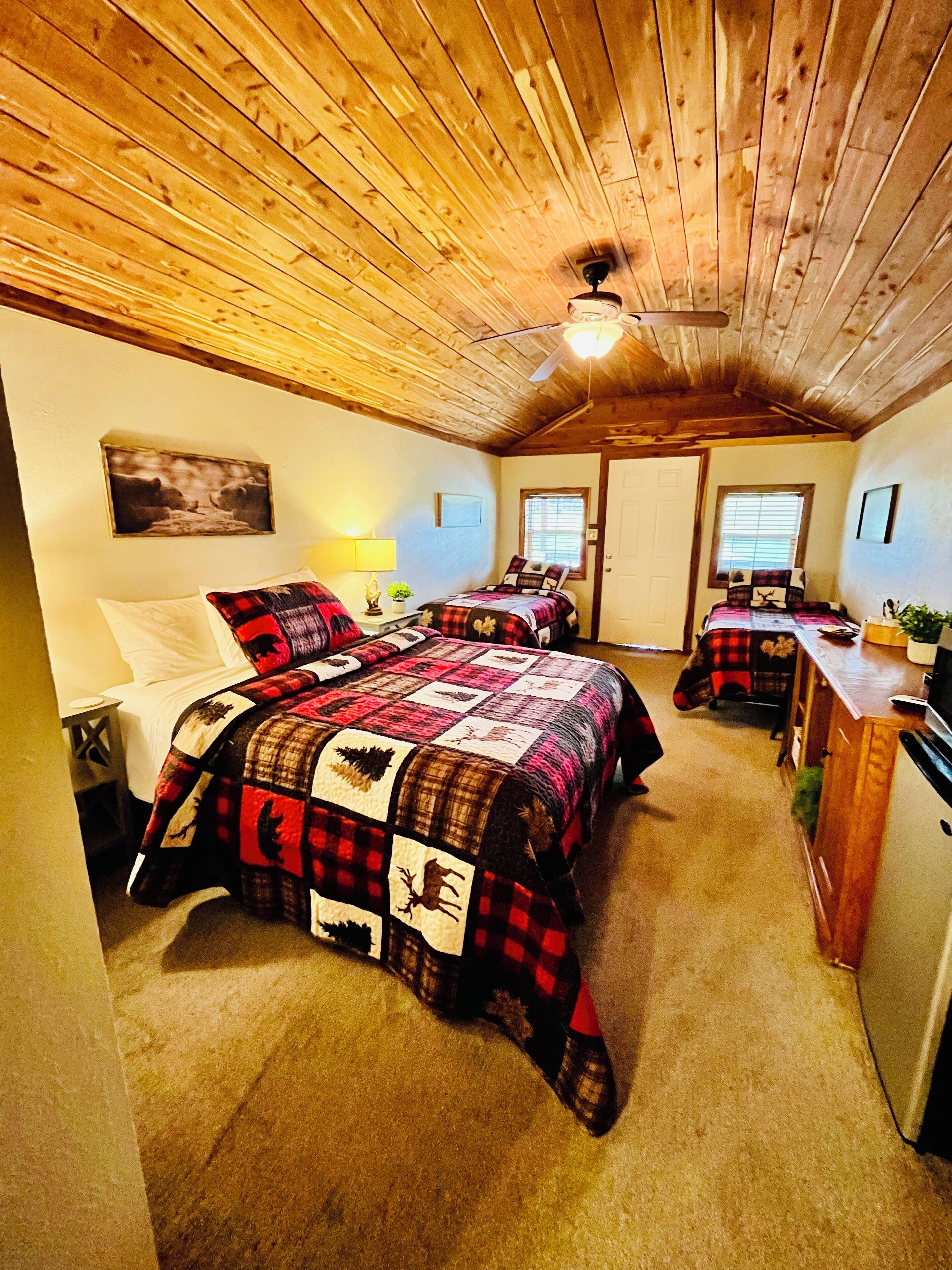 Un dormitorio acogedor con techo de madera, dos camas con colchas, un escritorio y una ventana.