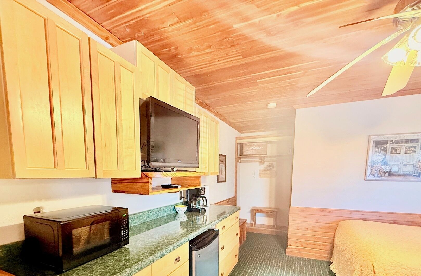 A compact kitchen with wooden cabinets, a microwave, a coffee maker, and a television.