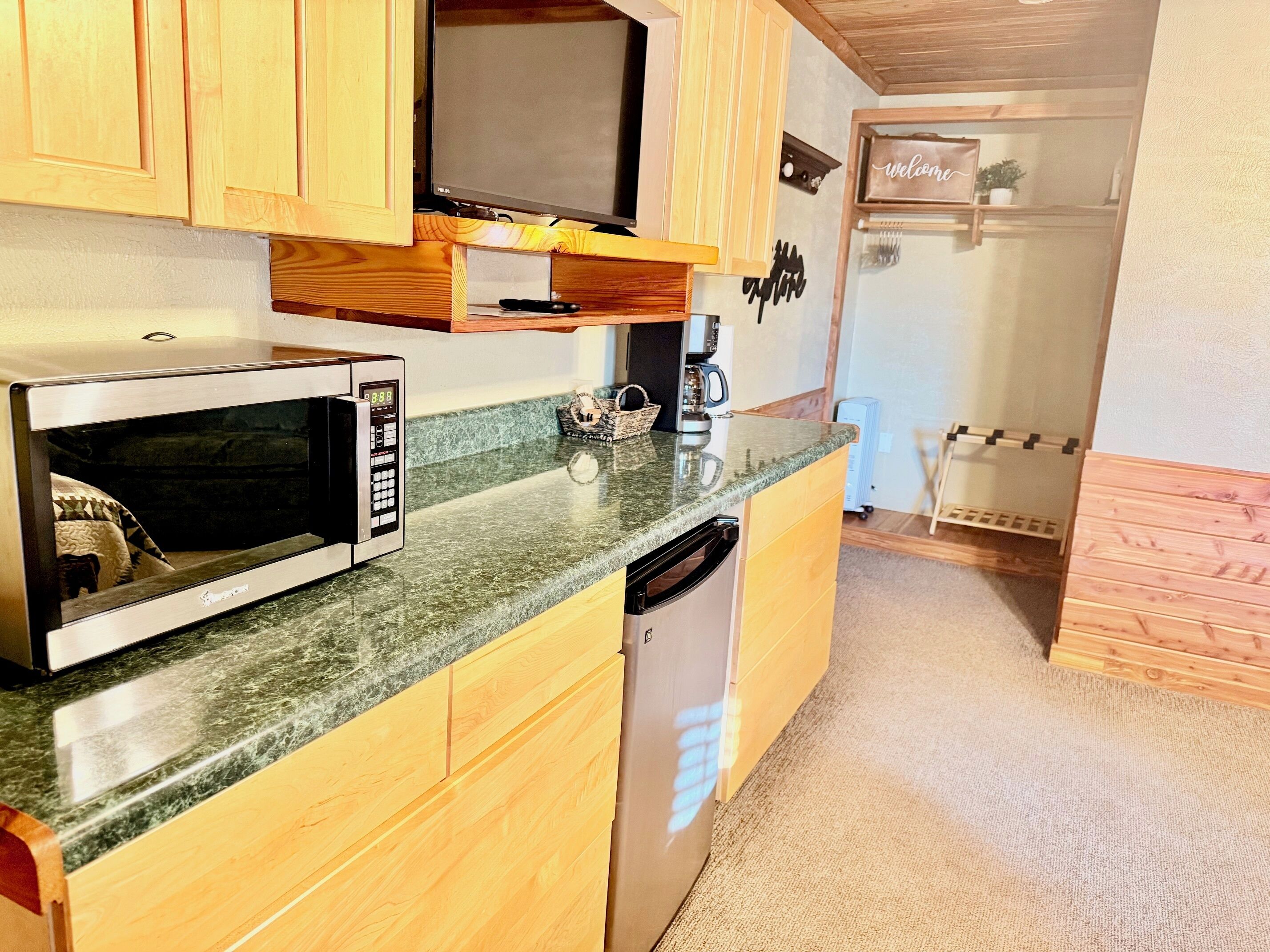 A compact kitchen with wooden cabinets, a microwave, a coffee maker, and a dishwasher.