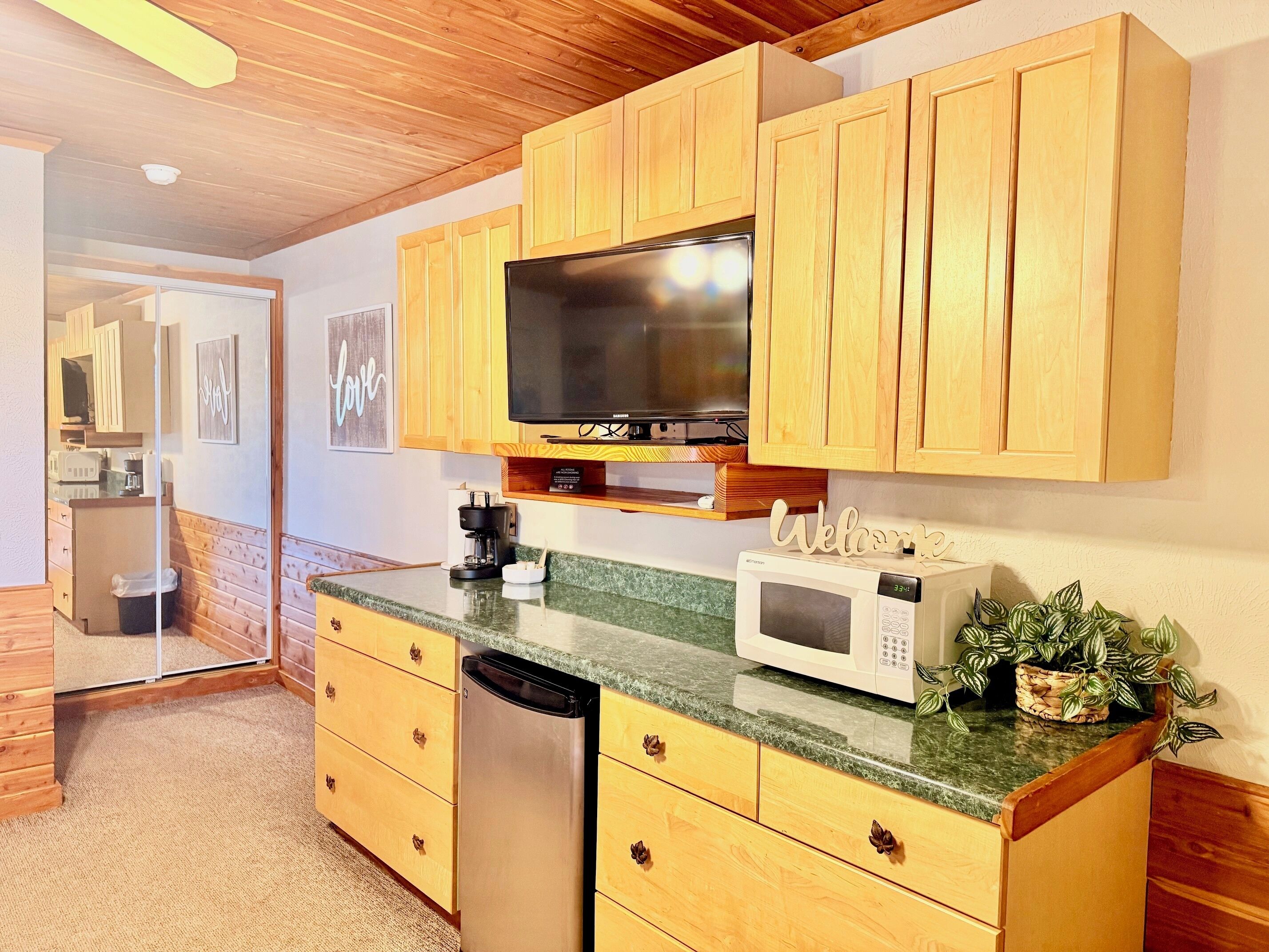 A kitchen with wooden cabinets, a microwave, a coffee maker, and a television.