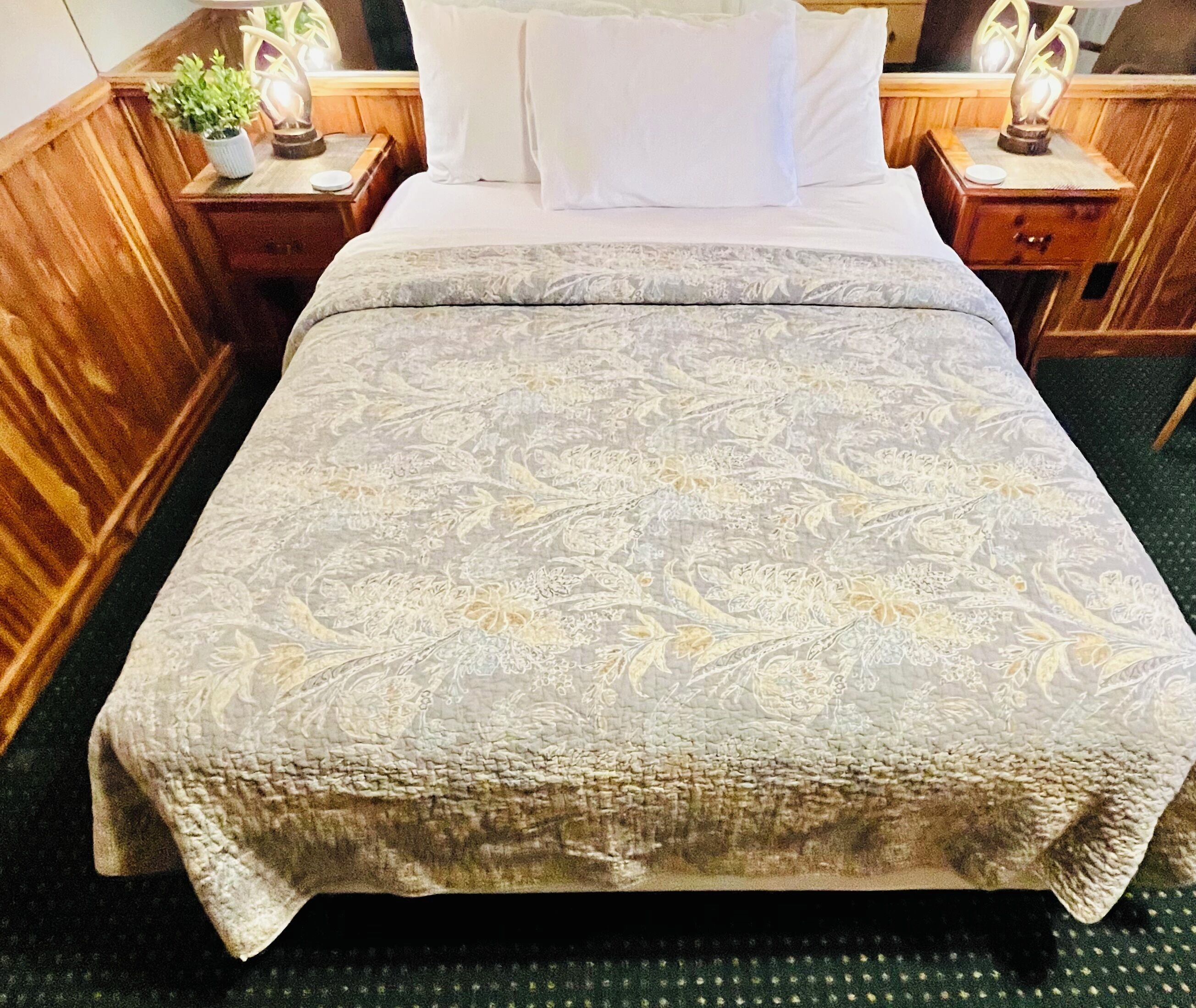 A bed with a patterned bedspread, wooden headboard, and two bedside tables with lamps.