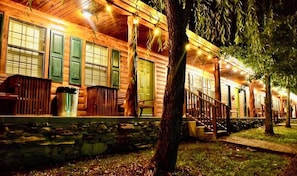 A wooden cabin with a stone foundation, a porch with wooden benches, and a green door. - Bear Inn Retreat (Clifton)