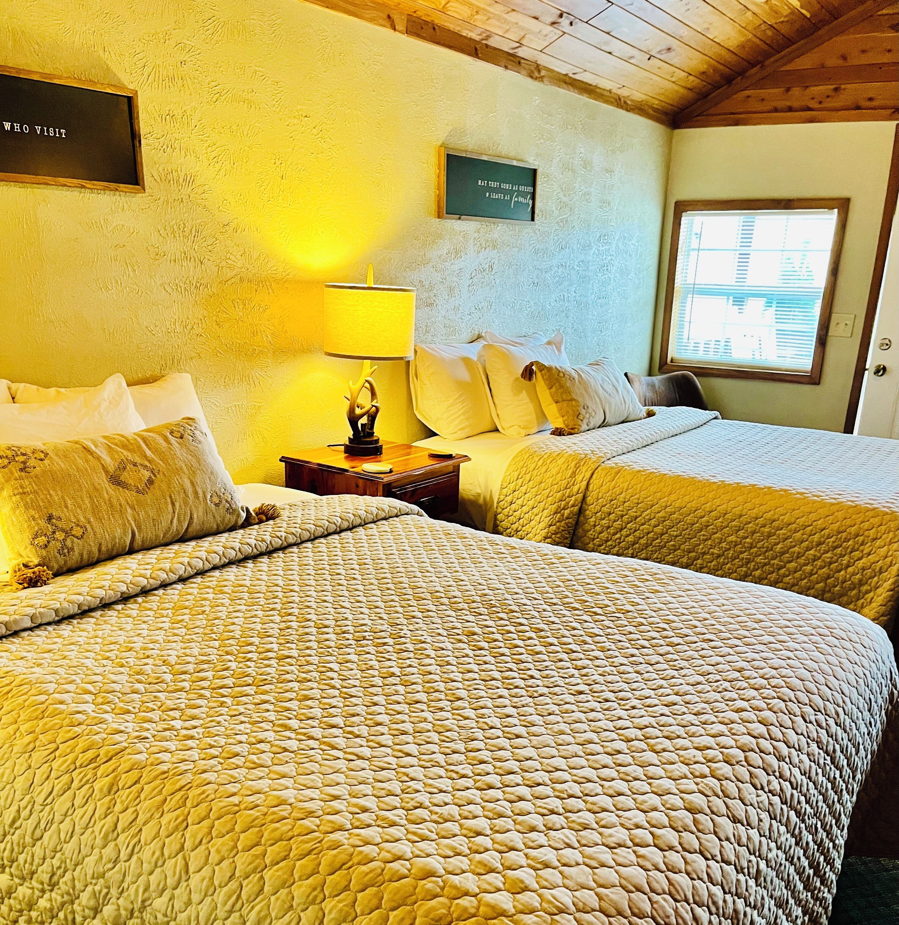 Une chambre avec deux lits, une table de chevet, une lampe et une fenêtre.