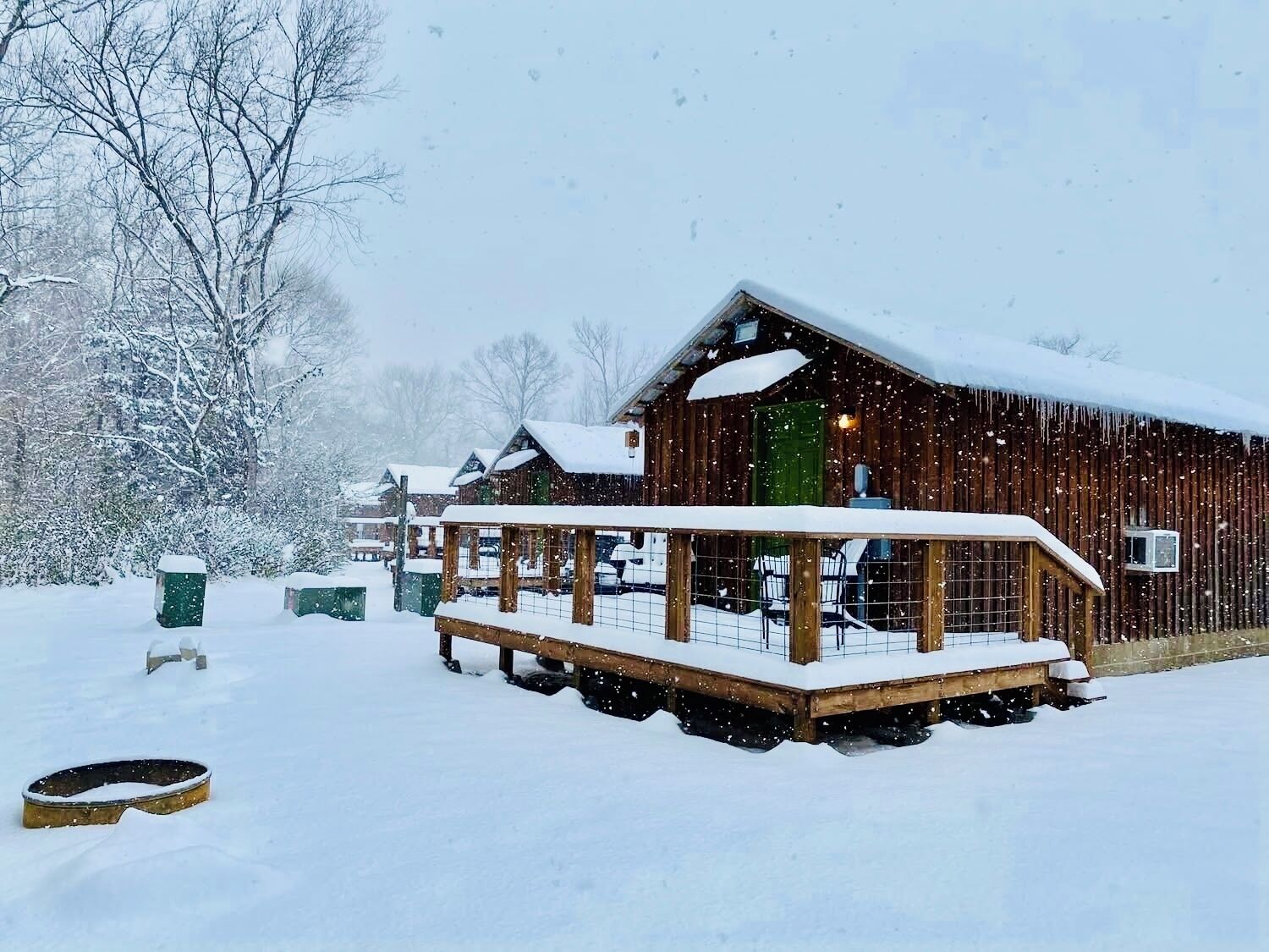 Une cabane en bois dotée d’un porche, entourée d’arbres couverts de neige.