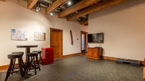 A room with a hexagonal tile floor, wooden beams, a red refrigerator, a wooden cabinet, and a television mounted on the wall. - Amazing Downtown Location. Sleeps 7. Dog Friendly (Fernie)