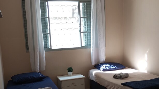 Een slaapkamer met twee bedden, een klein nachtkastje met een plant en een raam met gordijnen.