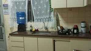 Een keuken met een spoelbak, aanrecht, kastjes en een raam met kantgordijnen.