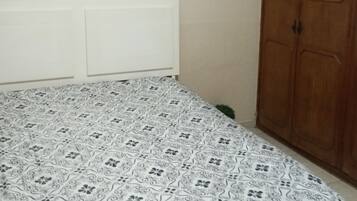 A bedroom with a patterned bedspread, a white headboard, and a wooden wardrobe.