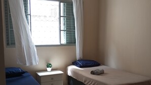 Slaapkamer met twee bedden, een klein nachtkastje, een bloempot en een raam met gordijnen.