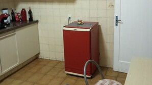 Een kleine keuken met witte kastjes, een rode koelkast en een tafeltje met twee stoelen.