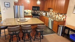 A kitchen with a central island, bar stools, wooden cabinets, a stainless steel refrigerator, a microwave, an oven, and a dishwasher. - 5 Min. Drive to the Resort & Fernie. Hot Tub (Fernie)