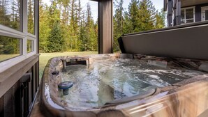 Un bain à remous avec vue sur une zone boisée, grâce à de grandes fenêtres.