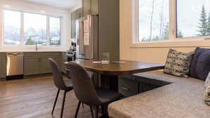 A modern kitchen with a built-in island, seating area, and large windows offering a view of trees. - Gorgeous 2 Bedroom with Private Hot Tub. A/C (Fernie)