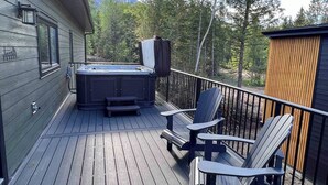 A wooden deck with a hot tub and Adirondack chairs, surrounded by trees and a mountain in the background. - Gorgeous 2 Bedroom with Private Hot Tub. A/C (Fernie)