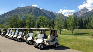 A row of golf carts parked on a road with a mountainous landscape in the background. - Gorgeous 2 Bedroom with Private Hot Tub. A/C (Fernie)