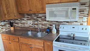 Une cuisine avec des meubles en bois, un évier en acier inoxydable, un four à micro-ondes blanc et une cuisinière blanche.