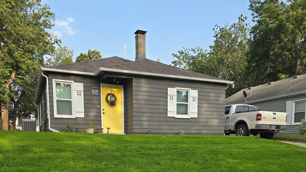 Une maison à deux étages avec une porte d’entrée jaune, une cheminée et une antenne parabolique.